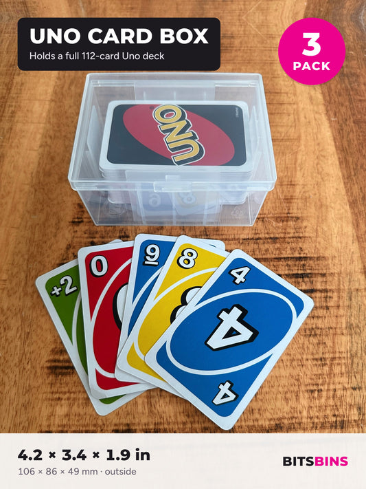 Uno card box 3 pack: a clear BitsBins case holding a full 112-card Uno deck, with Uno cards fanned out in front on a wood table.